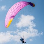 Experience the thrill of tandem paragliding with colorful parachute soaring high in the clear blue sky.